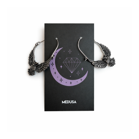 Silver earrings on a black card with 'Medusa' branding