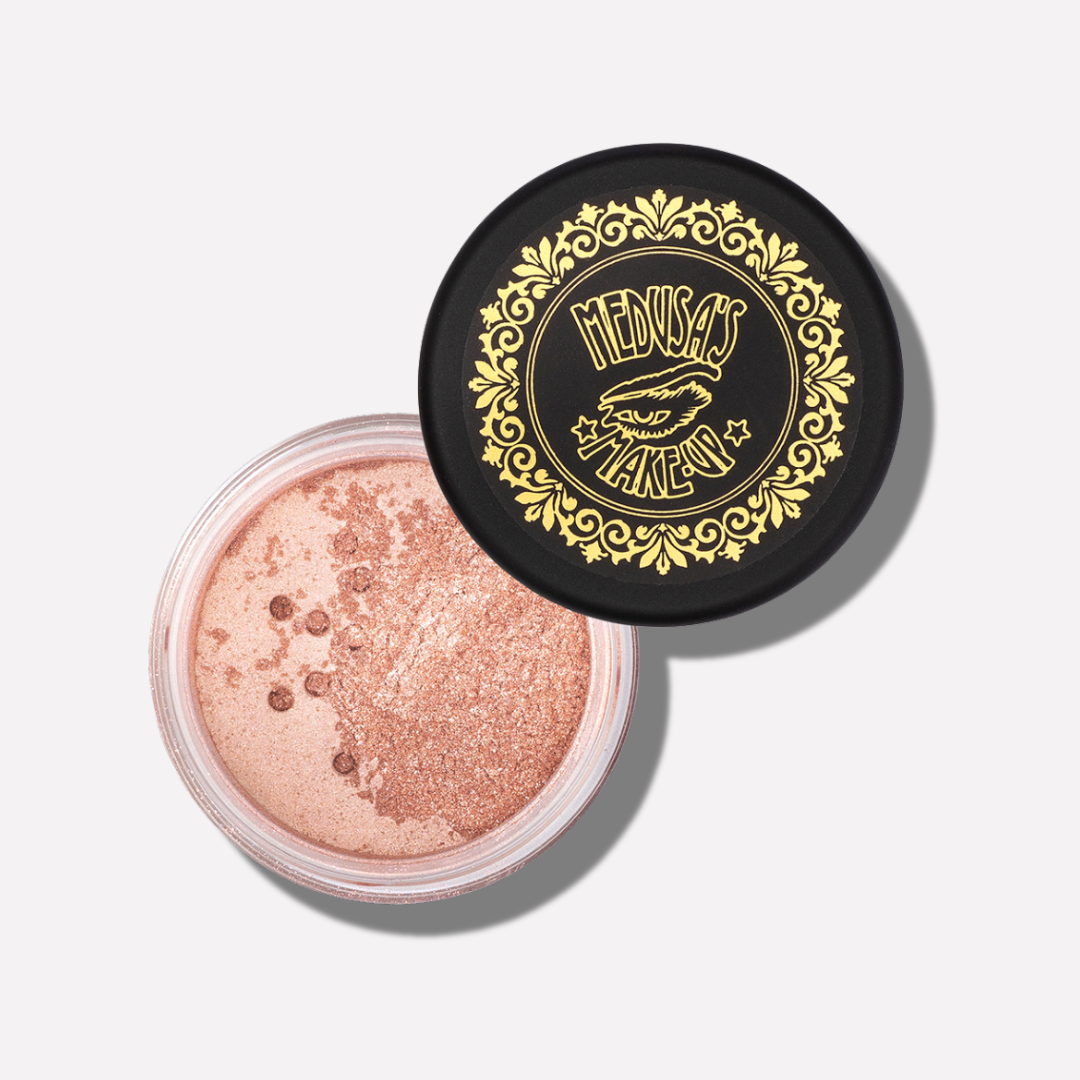 Open container of glittery powder with decorative lid featuring 'Medusa's Makeup' branding.