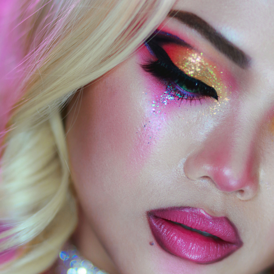 Close-up of a person with vibrant makeup, including pink and gold eye shadow and pink lipstick.