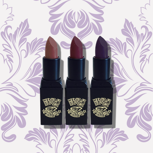 Three lipsticks with black cases on a decorative purple background