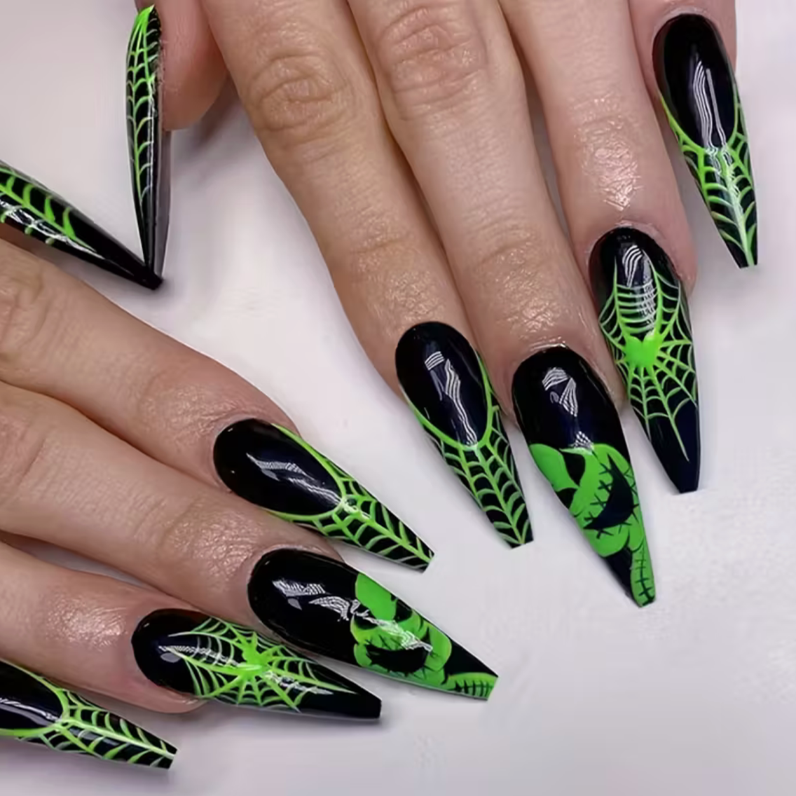 Nails with black and green spider web design on a white background