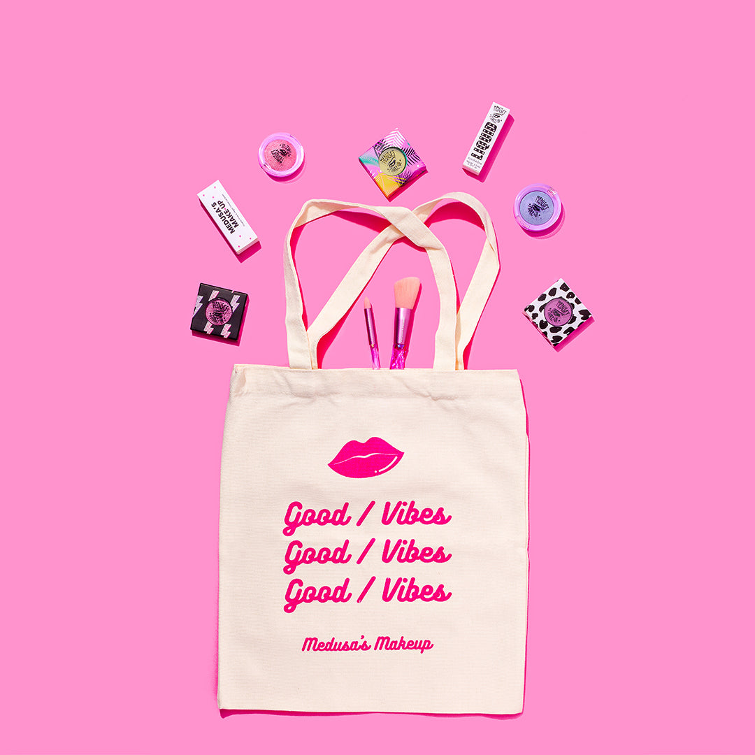 good vibes tote bag with makeup spread around on a pink background