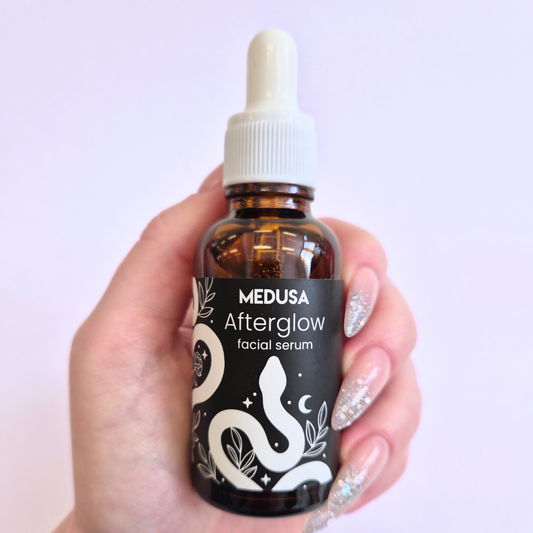 Hand holding a bottle of Medusa Afterglow facial serum against a light purple background