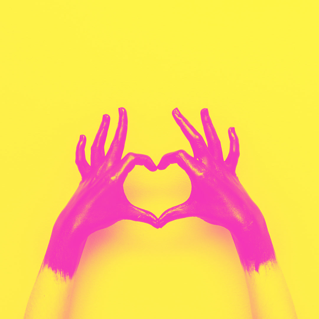 Pink hands making a heart sign on a yellow background