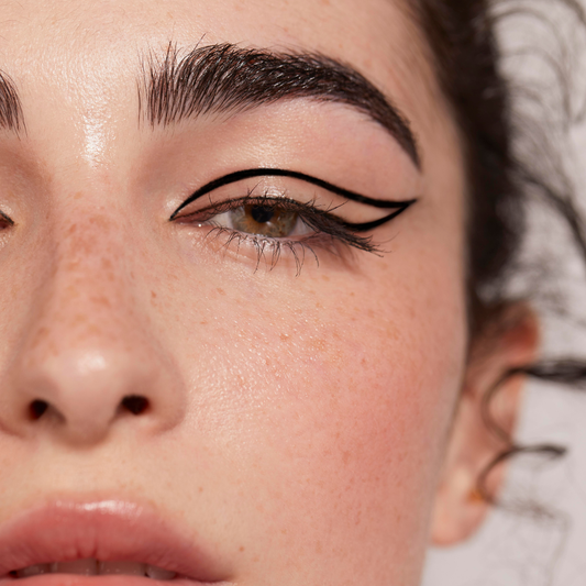 Close-up of a person's eye with cat-eye makeup on a neutral background