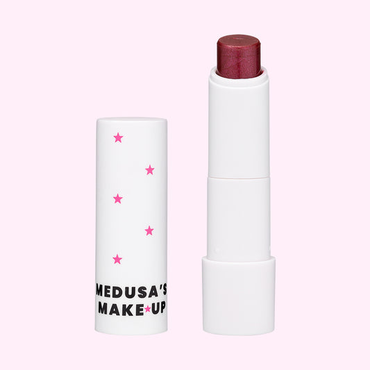 A vegan tinted lip balm by Medusa's Make-up, with the product slightly exposed showing a purple colored balm tip.