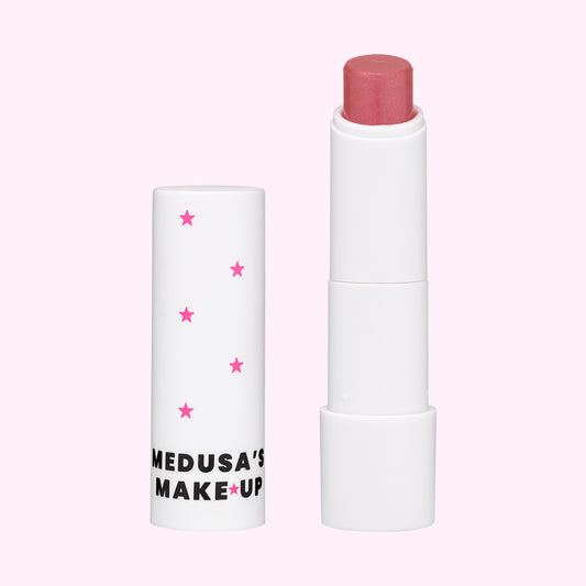 A white tube of Medusa's tinted lip balm with pink stars and text, containing a pink-colored lip balm stick.