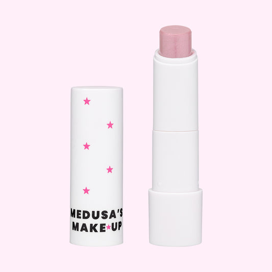 A stick of Medusa's vegan tinted lip balm with pink color, displayed next to its white packaging tube decorated with pink stars.