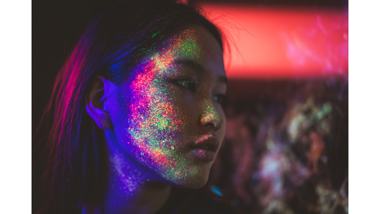 woman with neon makeup spattered across her cheek, under UV light