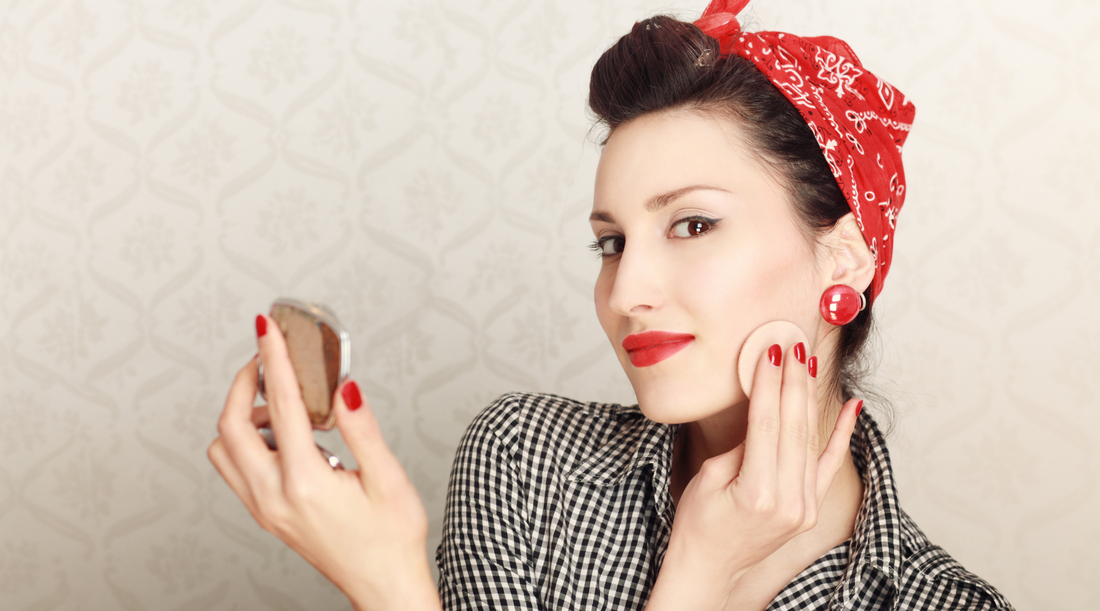 woman with vintage style hair, clothes, and accessories applying powder to her face