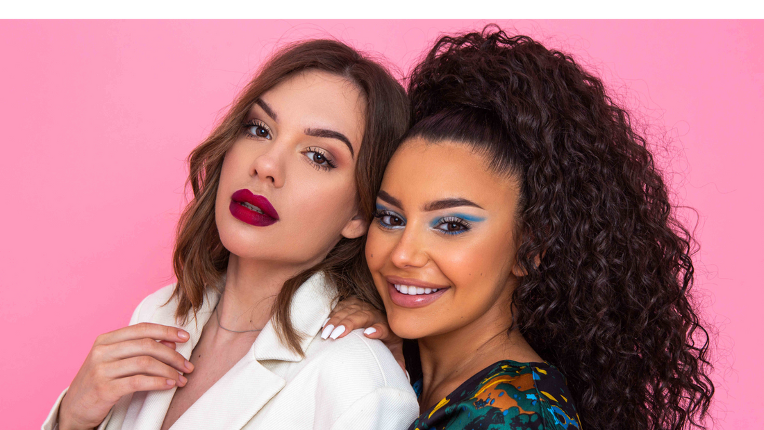 two women modeling makeup with a pink background