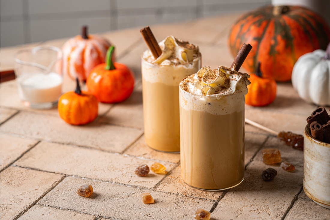 two pumpkin spice lattes sitting on a surface with pumpkins around them