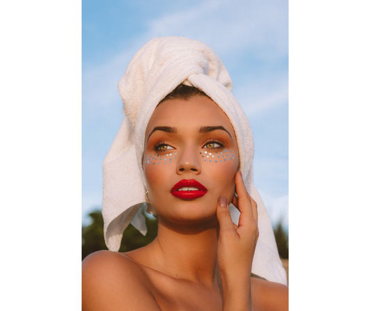 woman with her hair in a towel and glittery makeup with a red lipstick