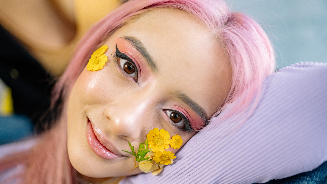 young woman with pastel pink hair leaning on her arm with pastel makeup and flowers on her cheeks