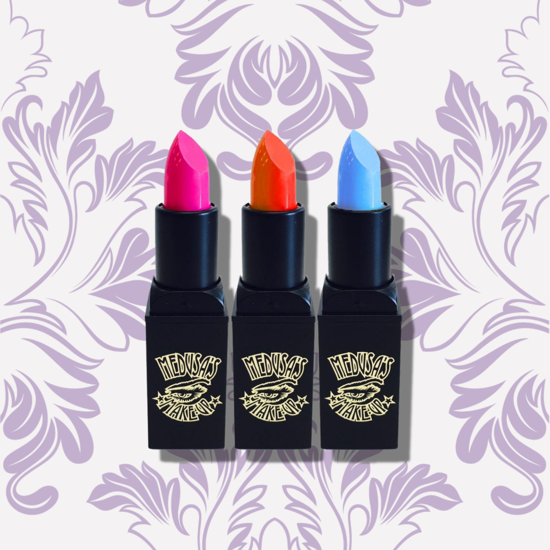 Three lipsticks with pink, orange, and blue shades on a decorative purple background.