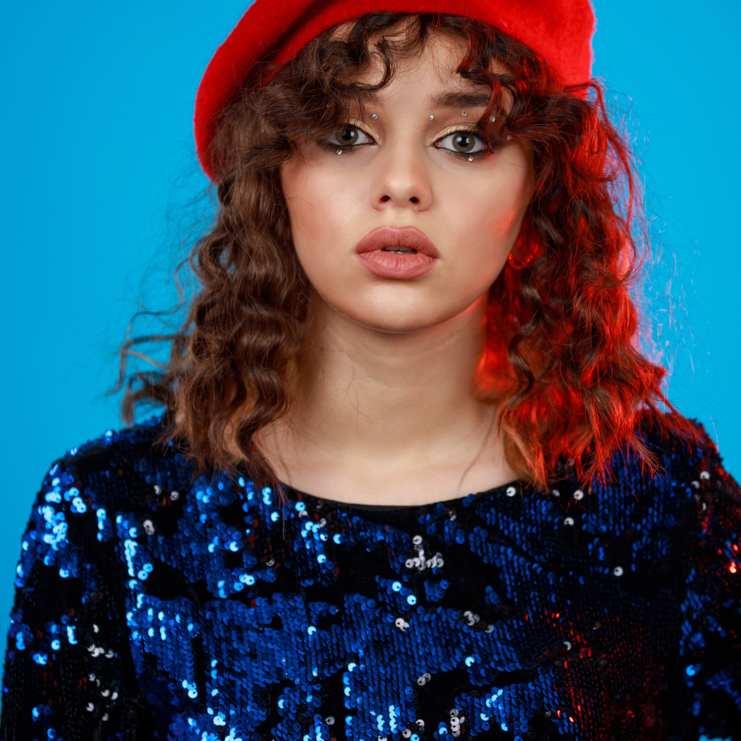Woman wearing a red hat and blue sequin top against a blue background