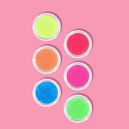 Six small containers of colorful glitter on a pink background