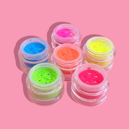 Set of six small jars filled with colorful glitter on a pink background