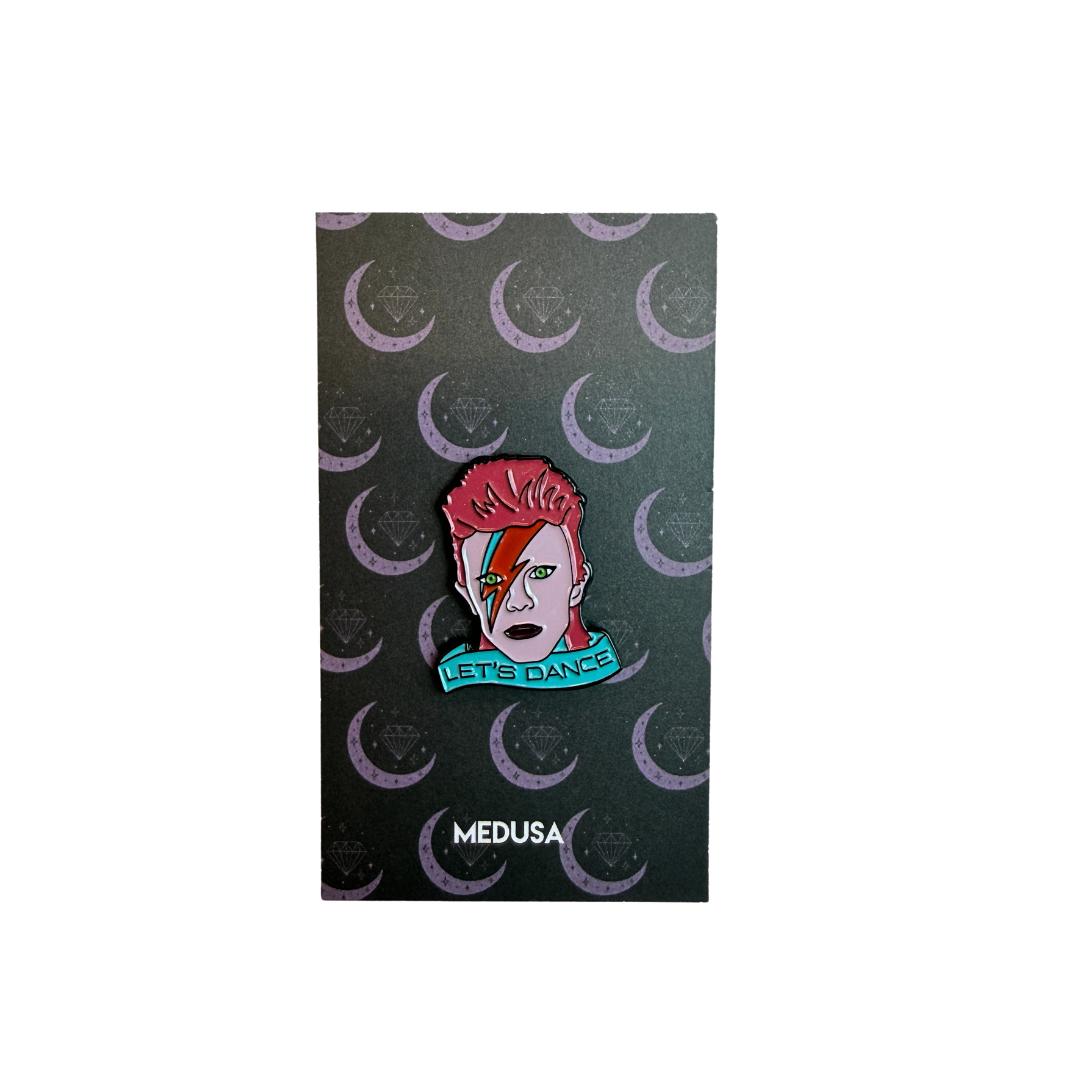 Pin with a design of a person with red hair and a rainbow, with 'Let's Dance' text, on a black background with crescent moon patterns. Brand 'MEDUSA' visible.