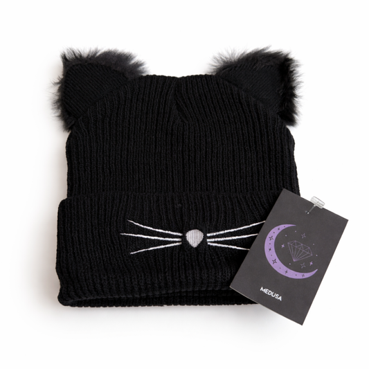 Black cat-themed beanie with pom-pom ears and a tag on a white background