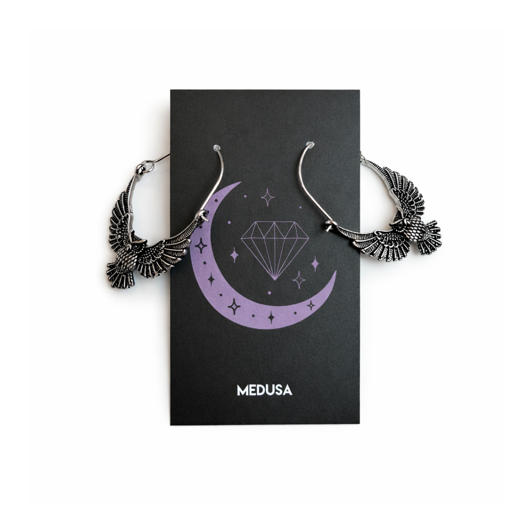 Silver earrings on a black card with 'Medusa' branding