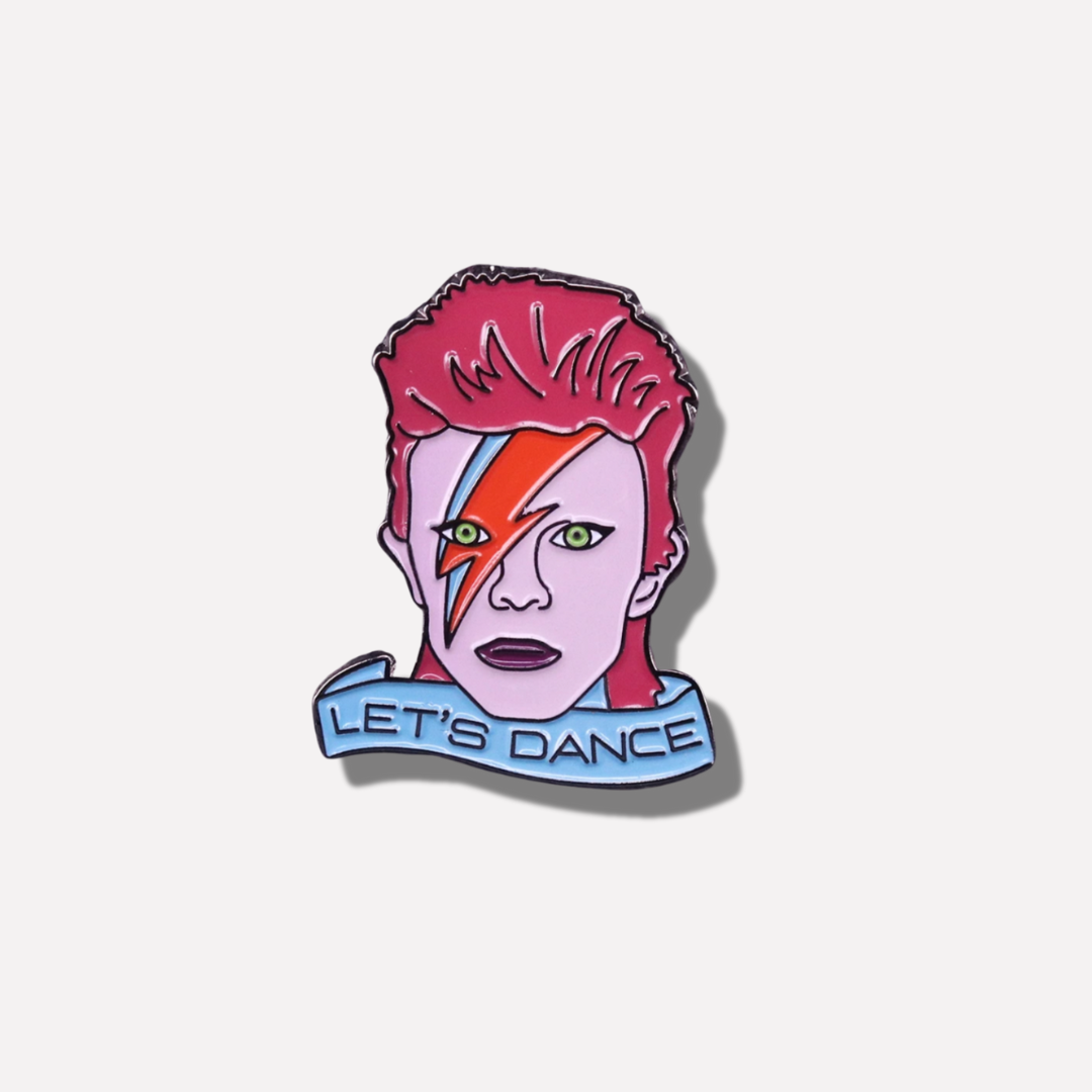 Enamel pin with a stylized face and 'Let's Dance' text on a light pink background