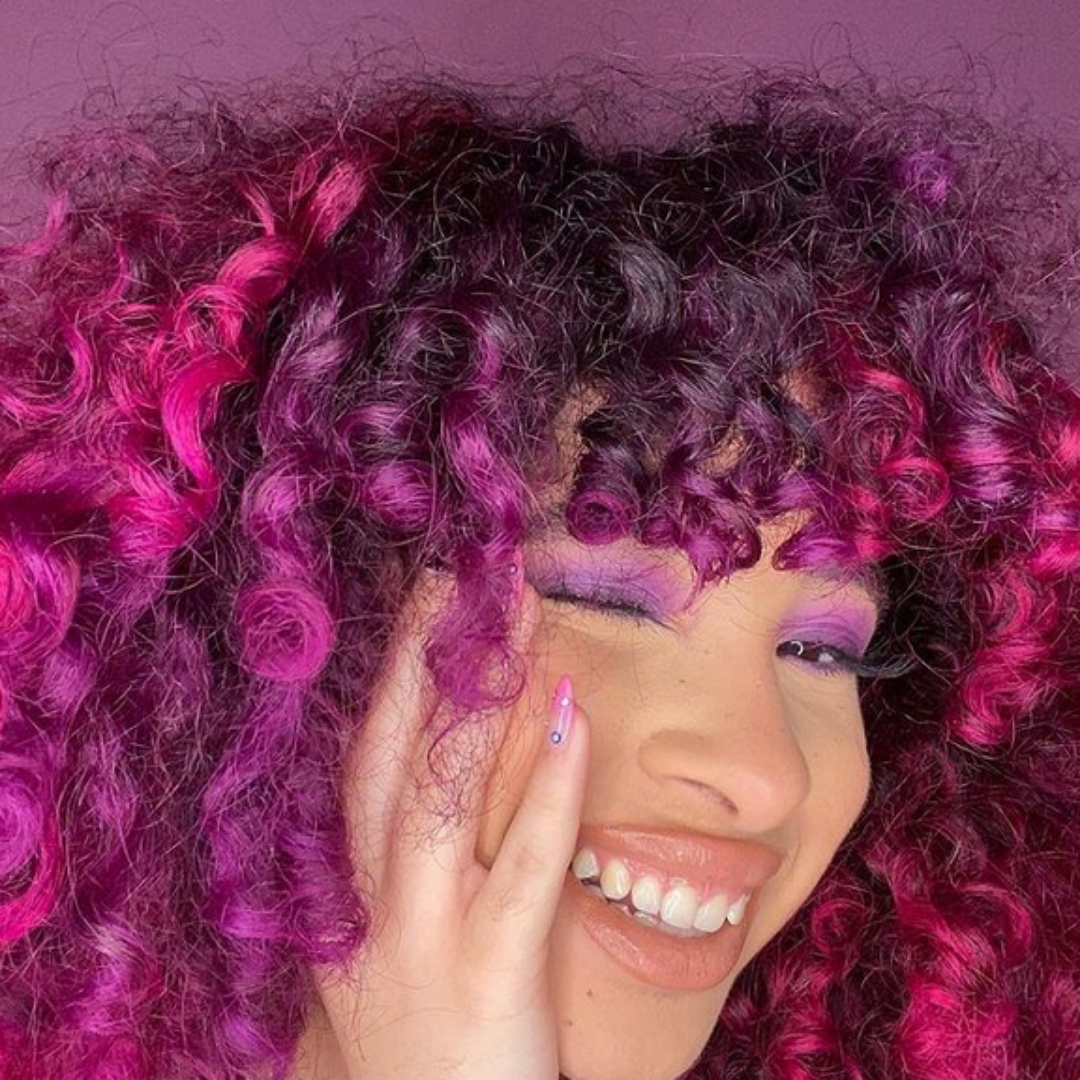 purple curly hair model wearing vibrant eyeshadow and nude lipstick