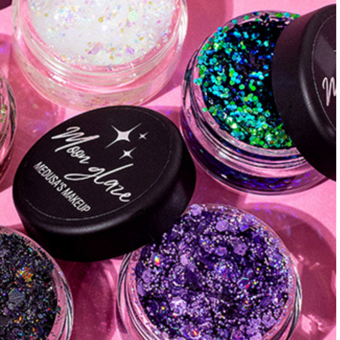 Glitter jars with colorful contents on a pink background, featuring the brand 'Medusa's Makeup'.