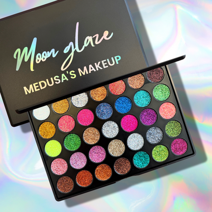 Makeup palette with colorful glittery shades and 'Moon Glaze' branding on a reflective surface.