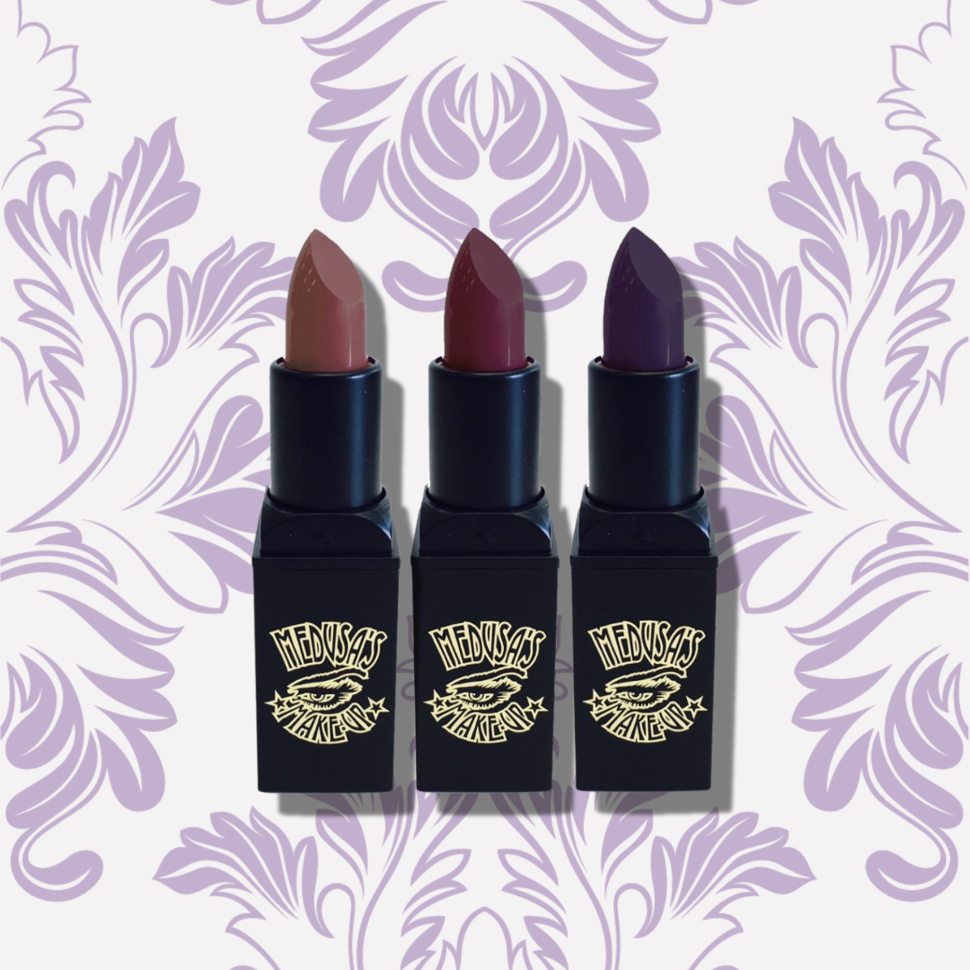 Three lipsticks with black cases on a decorative purple background