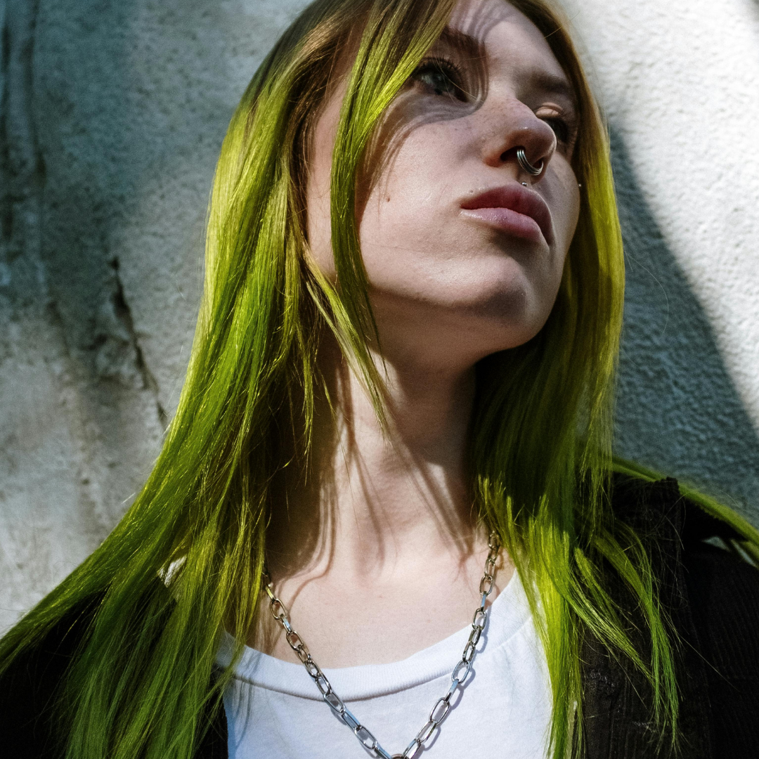 Person with green hair and a nose ring against a textured wall.
