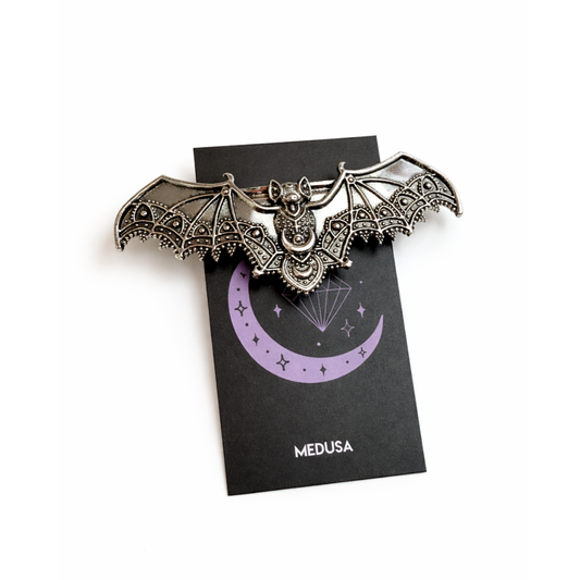 Bat-shaped brooch on a black card with 'Medusa' branding