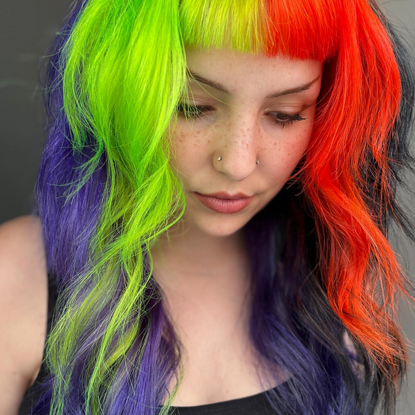 Person with multicolored hair looking downwards against a neutral background