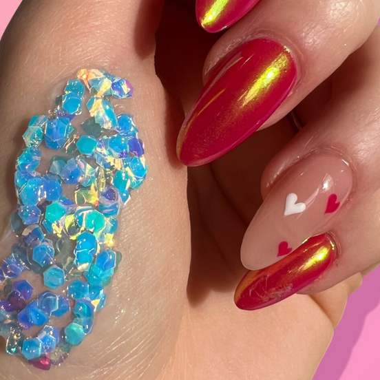 Close-up of a hand with colorful nail art and glitter on a pink background