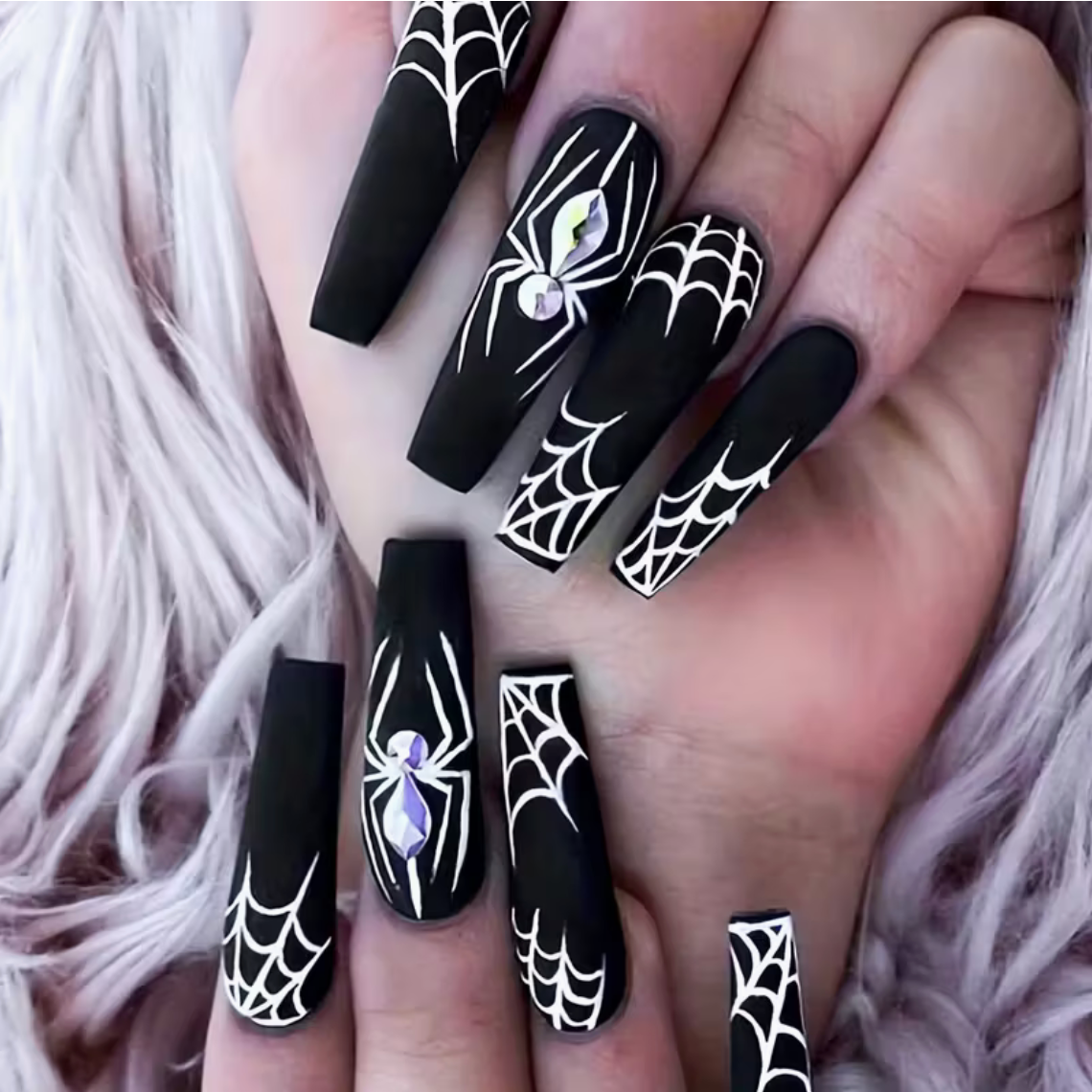 Black nails with spider and web designs on a hand with pink hair.