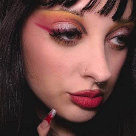 Close-up of a person with dramatic makeup and red nail polish.