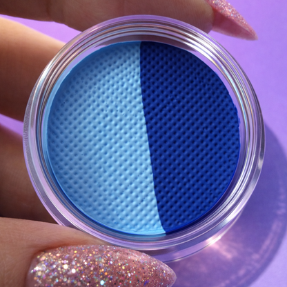 Two blue contact lenses in a clear container held by a hand with glittery nail polish on a purple background.