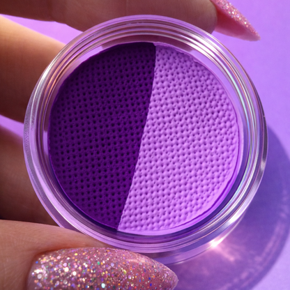 Purple contact lens case held by a hand with glittery nails on a purple background