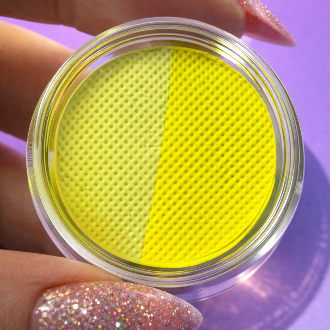 Two yellow makeup pads in a clear container held by a hand with glittery nail polish on a purple background.