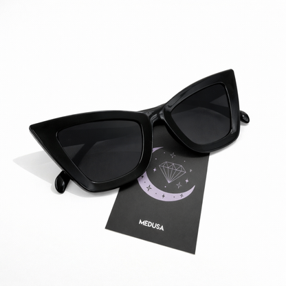 Black cat-eye sunglasses on a black card with 'Medusa' branding on a white background