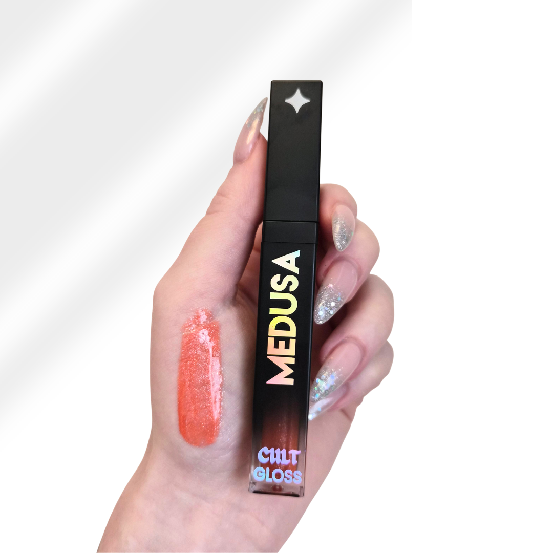 Hand holding a 'MEDUSA' lip gloss with visible color on the finger against a white background
