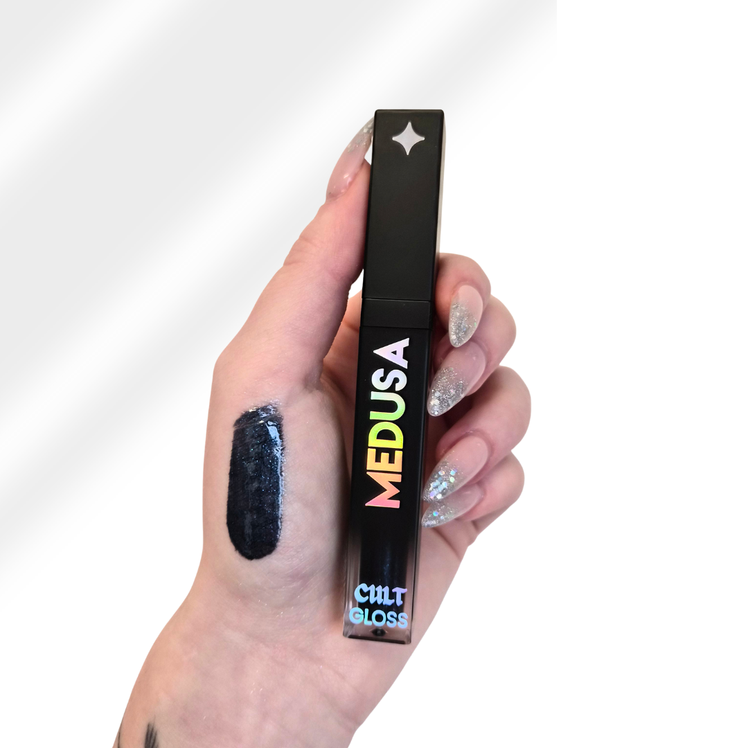 hand with lip gloss swatch in midnight blue holding a medusa lip gloss tube