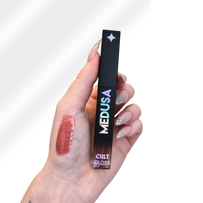 Hand holding a Cilt Medusa lip gloss with a swatch on the skin.