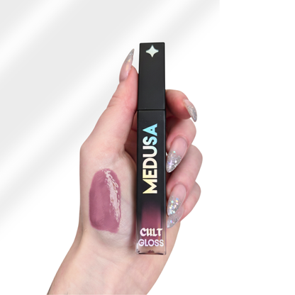 Hand holding a 'MEDUSA' lip gloss with a visible swatch on the skin.