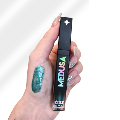 Hand holding a Cult Beauty Medusa lip gloss with a swatch on the skin.