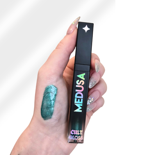 Hand holding a Cult Beauty Medusa lip gloss with a swatch on the skin.