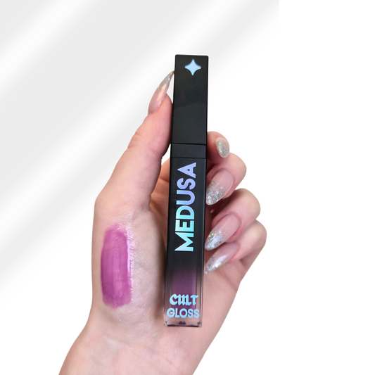 Hand holding a Cult Cosmetics Medusa lip gloss with a visible swatch on the skin.