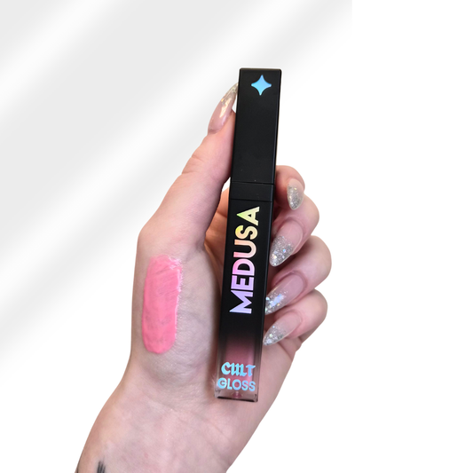 Hand holding a 'Medusa' Cult Gloss with pink lip gloss on a white background
