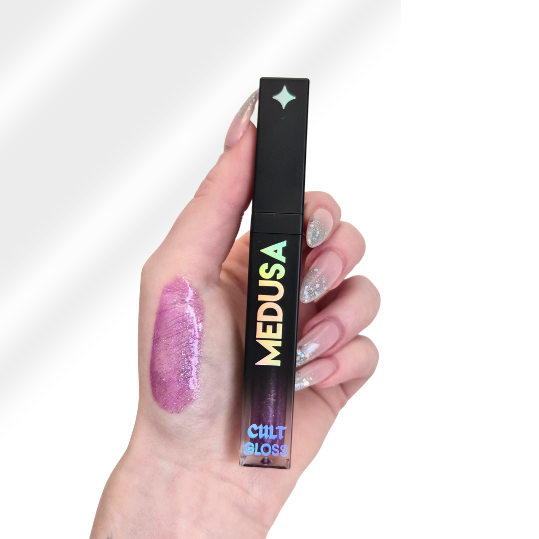Hand holding a 'MEDUSA' lip gloss with a swatch on the palm against a white background