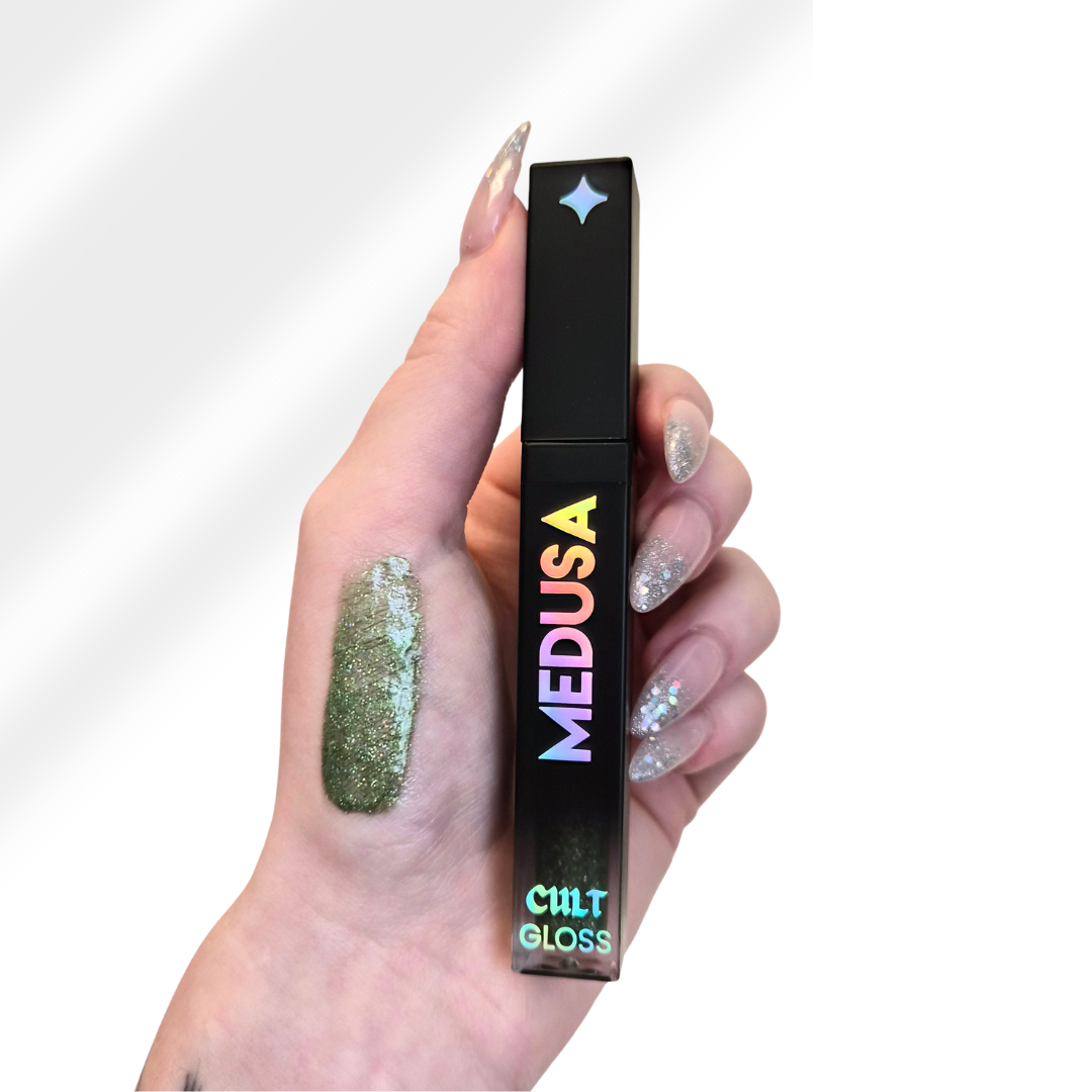 Hand holding a 'Medusa' Cult Gloss with green glittery lip color on a white background
